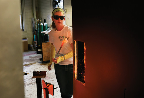 Mallory Purnell, a sophomore in ceramic engineering, removes her punty with molten glass from the glory hole before returning to the work bench to shape her piece.