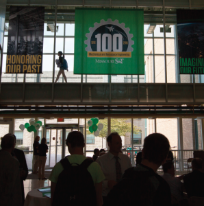 Three banners hung from the ceiling. Banner on the left has a black and white historic image with the words "Honoring our past"; Center banner is green with the 100th anniversary mark; Right banner with an image of the earth taken from space with the words "Imagining our future."