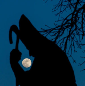 Evening shot of the St. Patrick statue in a silhouette with the moon framed between the arm and head.
