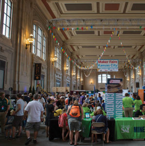 Standing at one end of the Kansas City Union Station hall looking down at opposite end. Crowds gather around different interactive booths engaging in activities. Missouri S&amp;T tables to the right with vertical mission control banners behind the tables.