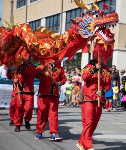 Four S&amp;T students dressed in traditional Chinese attire walk in a parade carrying a long dragon puppet above their head.