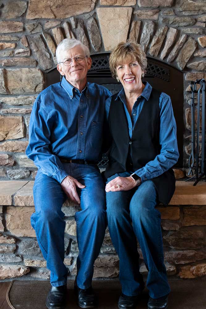 Joan Woodard sits to the right of her husband in front of the stone fireplace in their home.