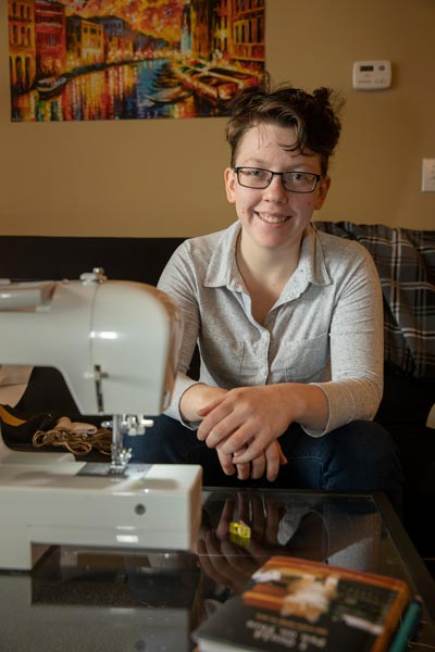 Portrait of Laurie sitting on her couch with a sewing machine on a coffee table in front of her.